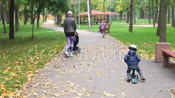 小男孩骑着滑板车骑着平衡车骑在柏油路旁妈妈在城市公园附近散步视频的预览图