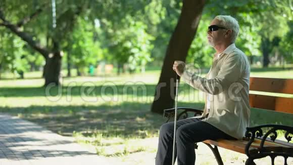 老盲人从长凳上站起来用拐杖在公园里散步清理道路视频的预览图