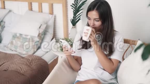 漂亮的女孩坐在草椅上用电话喝茶慢动作视频的预览图