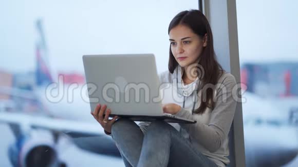在机场窗口附近的笔记本电脑上工作的女人背景模糊的飞机视频的预览图