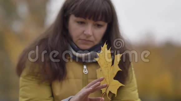 伤心的女人手里拿着枫叶在秋天的户外慢动作中想着什么视频的预览图