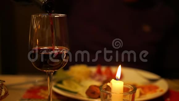 在蜡烛特写镜头下人们将美味的红酒倒入酒杯中视频的预览图