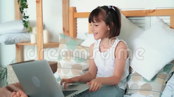 女孩坐在床上使用笔记本电脑玩电脑游戏慢动作视频的预览图