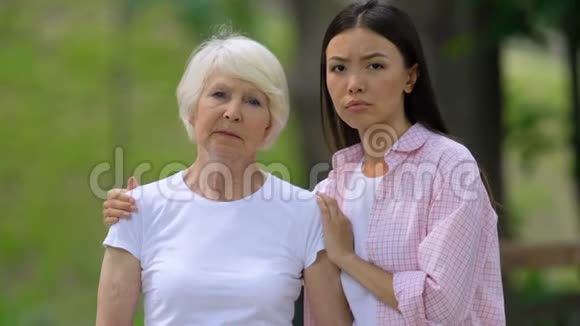 心烦意乱的年轻女子和外婆在户外看着摄像机社会支持视频的预览图