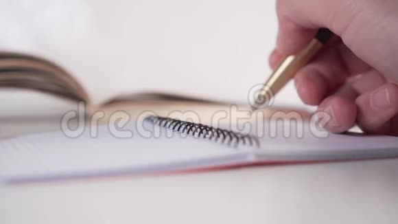 一个年轻人用金笔在计划者的书桌上用黑色的螺旋纸写字背景是一本书视频的预览图
