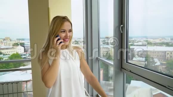 年轻女子在宽敞的房间里用手机交谈背景是城市景观视频的预览图