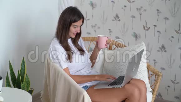 女自由职业者坐在草椅上喝茶用笔记本电脑工作动作缓慢视频的预览图