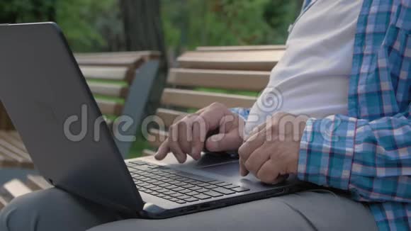 公园里老人用电脑的特写镜头他正在触摸触摸板浏览互联网视频的预览图