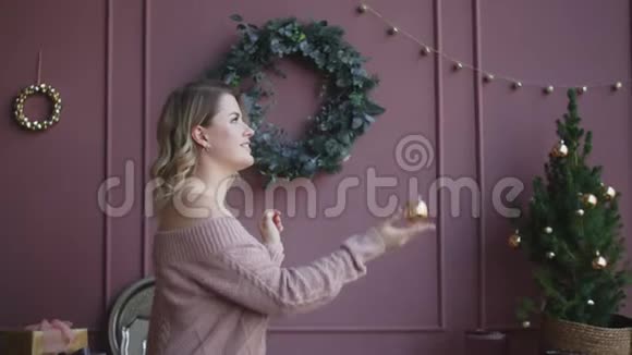 穿着毛衣的漂亮女人慢慢地举起一个圣诞球装饰圣诞树舒适的新年家视频的预览图