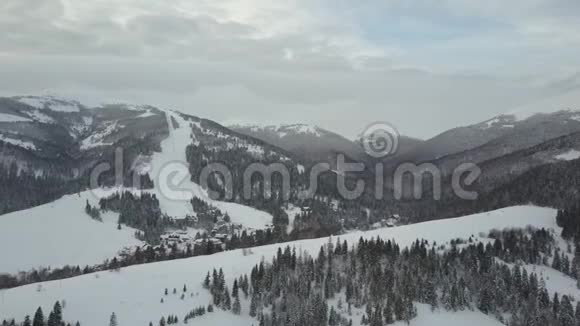 飞越喀尔巴阡山脉的一个村庄和它旁边的一个滑雪胜地鸟瞰白雪覆盖的房屋视频的预览图