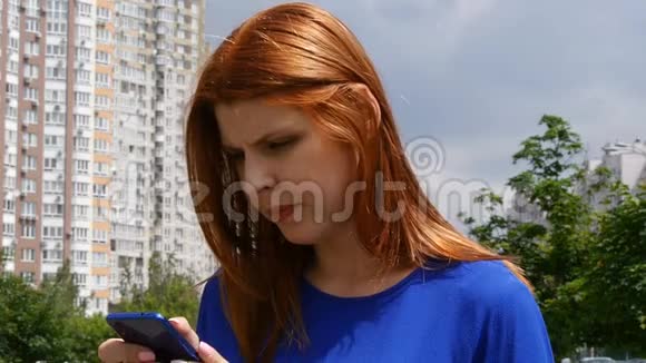 年轻漂亮的红发女孩在城市里在手机里找到了信息微笑着视频的预览图