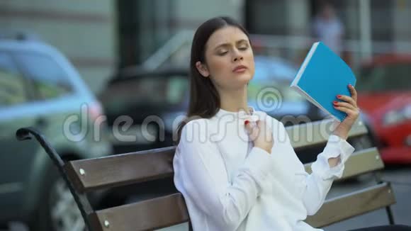 坐在长凳上的女人拿着笔记本挥舞着在炎热的天气条件下感到恶心视频的预览图
