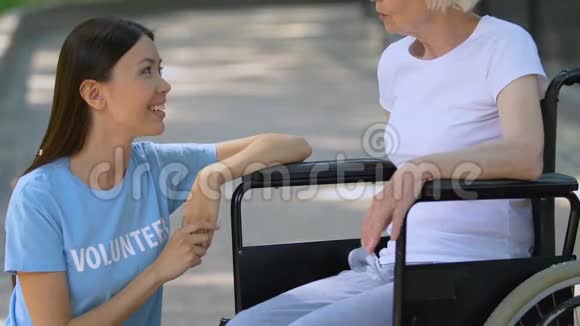 微笑志愿者与轮椅上的老年女性患者交谈公园放松视频的预览图
