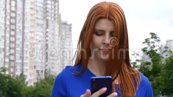 年轻漂亮的红发女孩在夏天穿过城市在电话里交谈视频的预览图
