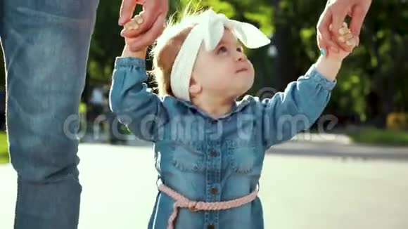 可爱的学步女孩在阳光明媚的公园里散步父母牵着她的手视频的预览图