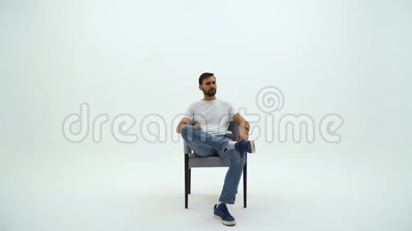 英俊的胡子男人穿着白色的t恤椅子在白色的背景上人从椅子上站起来离开视频的预览图