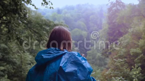 穿着蓝色雨衣的女孩在森林里拍照视频的预览图