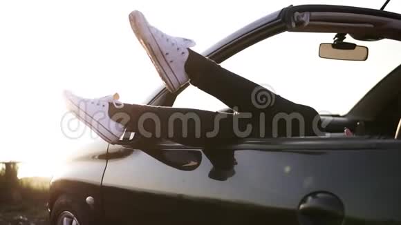 快乐的年轻女人休息把她的白色运动鞋从敞篷车黑色汽车温和的夏日阳光视频的预览图