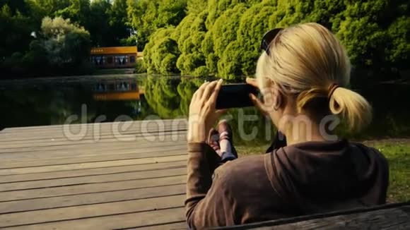 快乐的女人在公园的池塘边放松拍照视频的预览图
