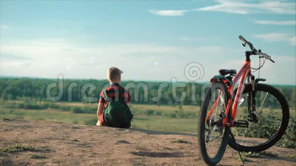 穿着红色T恤背着背包的少年在日落时分坐在高山上享受自然自由视频的预览图