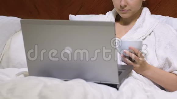 漂亮的女商务小姐穿着浴袍喝着茶在酒店工作手提电脑视频的预览图