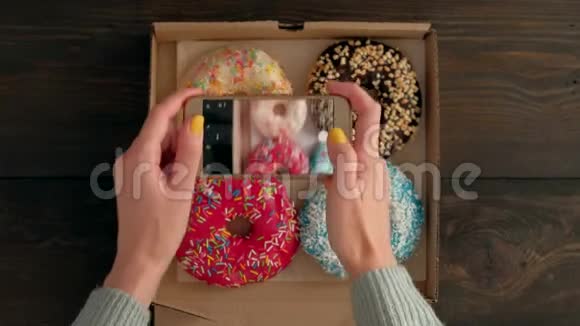女人手拿着智能手机在盒子里拍美味的甜甜圈视频的预览图