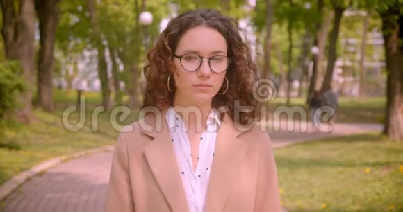 戴眼镜的白种人年轻的长头发卷发女学生的特写肖像双臂交叉在胸前视频的预览图