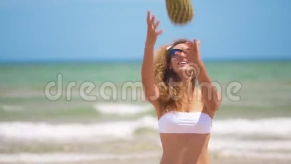 有趣的微笑女孩在夏季泳装和太阳镜性感女孩把菠萝扔在美丽的背景上视频的预览图