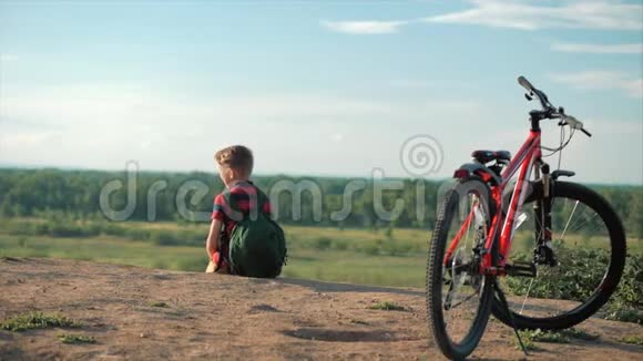 穿着红色T恤背着背包的少年在日落时分坐在高山上享受自然自由视频的预览图