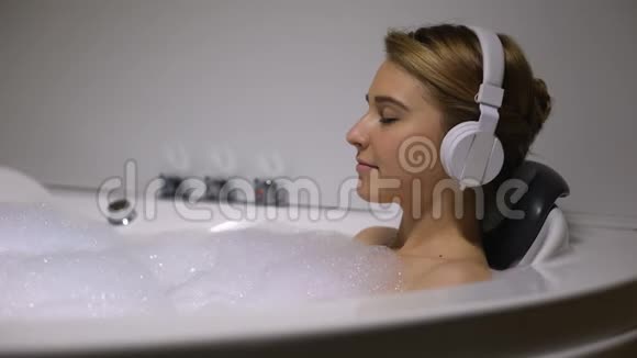 戴着耳机的女人在泡着泡沫的浴缸里听着慢音乐视频的预览图