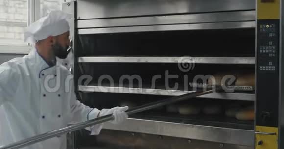 特写面包师从烤箱中取出烘焙面包用一个特殊的火炬卸下货架视频的预览图