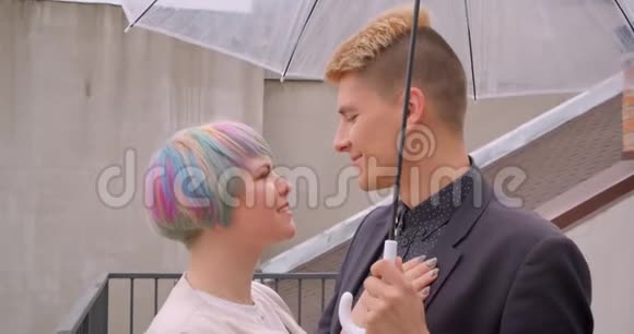 一对年轻漂亮的时髦情侣在伞下站在一起看着对方开心的特写镜头视频的预览图