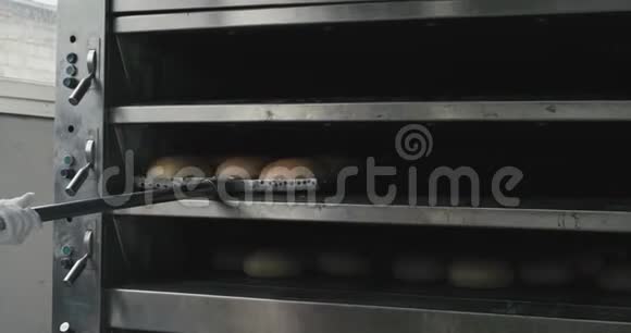 一位带着白手套的面包师厨师从烤炉机上取出烤面包并将其卸在货架上视频的预览图