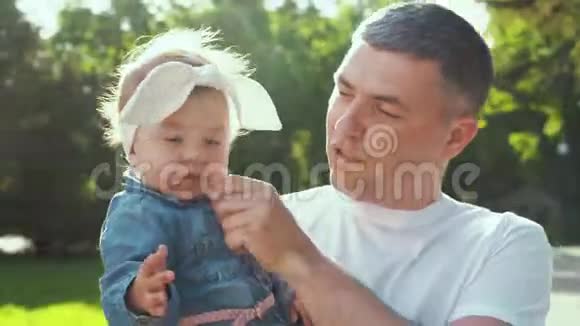 阳光明媚快乐的父亲抱着他的宝贝女儿在夏天公园散步视频的预览图