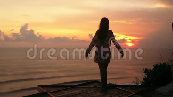女孩张开双臂在海滩上看日落和大海慢动作视频的预览图