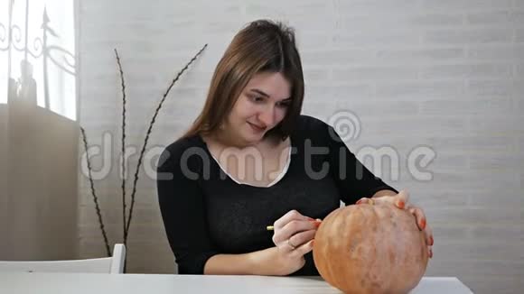 万圣节的概念快乐的女孩坐在一张桌子上用南瓜画眼睛和嘴巴视频的预览图