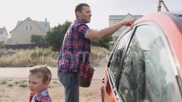 可爱的父亲教他的小男孩如何缓慢地洗车视频的预览图