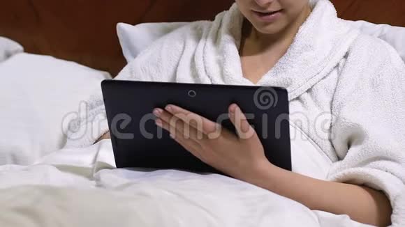 漂亮的女士在平板电脑上打字躺在床上使用网上银行应用程序视频的预览图