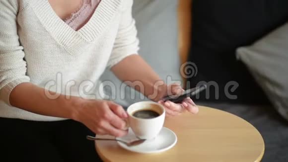 女人在餐桌上写作喝咖啡或茶她端着杯子看着智能手机特写视频的预览图