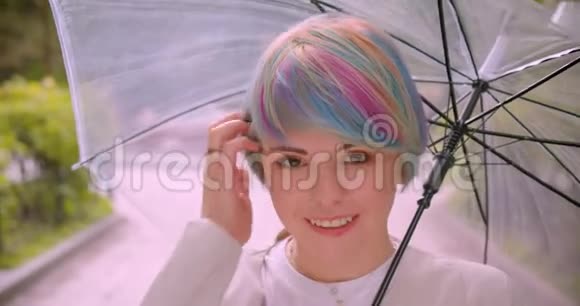 一位年轻可爱的白种人女性的特写照片她染着头发拿着雨伞看着相机修头发视频的预览图