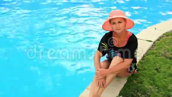 阳光明媚的夏日戴着太阳帽的年轻美女坐在池边享受着美好的一天和心情视频的预览图
