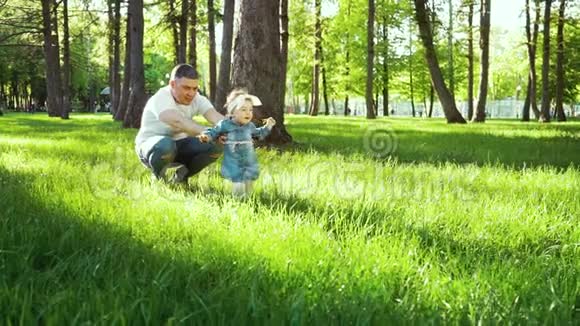 快乐的父母看着他们的宝贝女儿在花园的绿草上迈出第一步视频的预览图