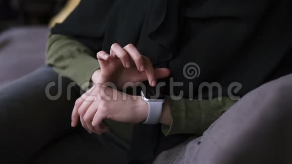 穿着黑色头巾的阿拉伯女人独自坐在现代咖啡馆里用她的智能手表用手指滑动数据慢慢视频的预览图