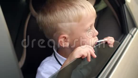 小男孩拿着棒棒糖坐在车里他看着车窗外视频的预览图