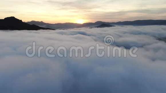 日落时分在山峰下面的浓密的云层上进行空中飞行视频的预览图