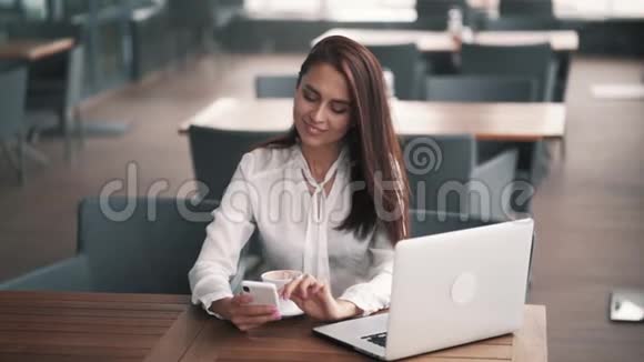 漂亮的女商人用智能手机和笔记本电脑在咖啡馆工作慢动作视频的预览图