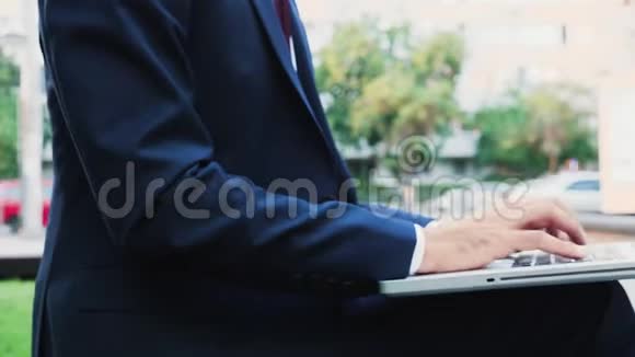 在城市户外的笔记本电脑键盘上打字时穿着商务套装的经理关闭放大镜头视频的预览图