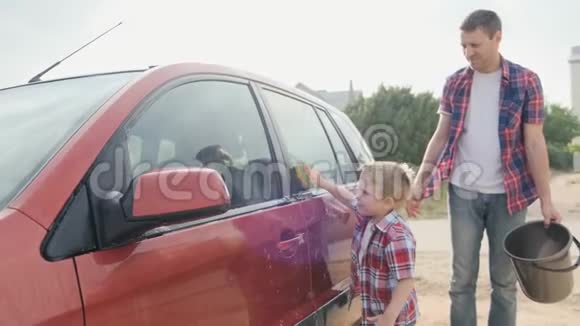 爸爸和小儿子穿着格子衬衫慢动作地洗红色汽车视频的预览图