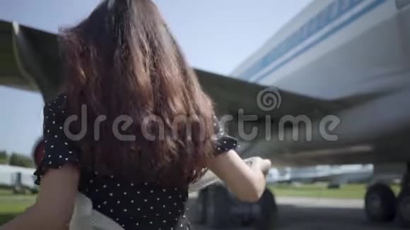 年轻的黑发女孩戴着白色披肩和太阳镜在大飞机前旋转看着相机视频的预览图