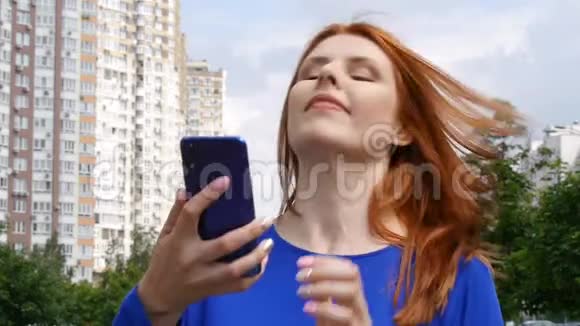 一个年轻漂亮的红发女孩在城市里走来走去接着手机的电话很高兴视频的预览图